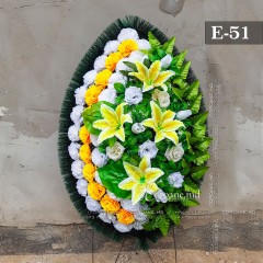 Coroana funerara originală 100cm din flori artificiale. Flori: garoafe albe, garoafe galbene, trandafiri albi, crini galbeni. Frunziş: ferigă. Carcasă: cetină.