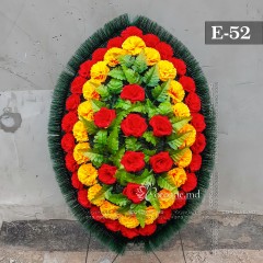 Coroana funerara originală 100cm din flori artificiale. Flori: garoafe roşii, garoafe galbene, trandafiri roşii. Frunziş: ferigă. Carcasă: cetină.