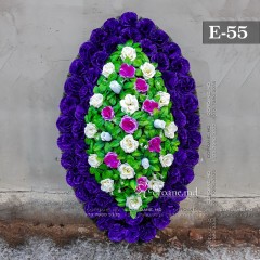 Coroana funerara originală 120cm din flori artificiale. Flori: garoafe violete, trandafiri mov, trandafiri albi. Frunziş: ferigă. Carcasă: cetină.